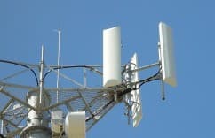 Cell tower with antennas and cables against a clear blue sky with clouds.