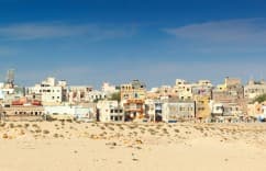 City skyline with buildings and a cell tower under a clear blue sky.