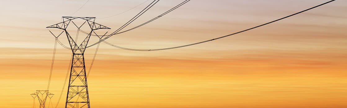 Power line tower silhouette against an orange sunset sky.