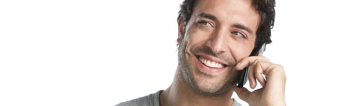 Man in a gray shirt smiling and talking on a mobile phone against a white background