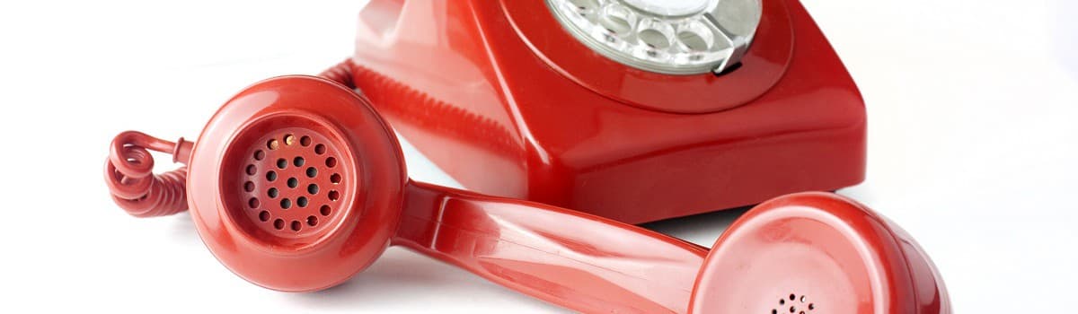 Red vintage rotary telephone with a coiled cord on a white background.