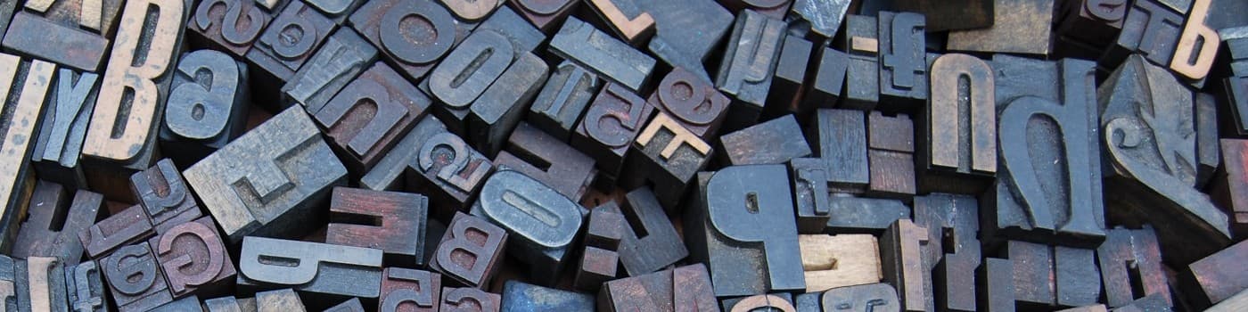 Pile of assorted letterpress blocks with letters and numbers in various shades of gray and brown.