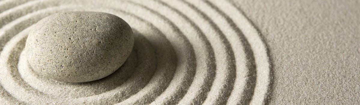 Smooth gray stone on raked sand with concentric circular patterns.