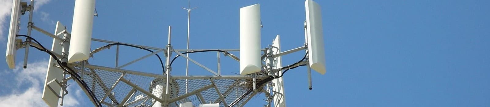 Cell tower with antennas and cables against a clear blue sky with clouds.
