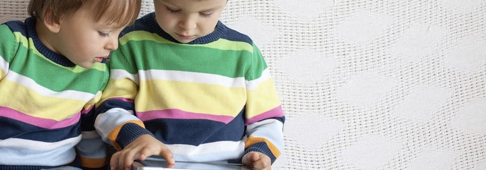 Two children wearing identical jumpers, looking at a tablet